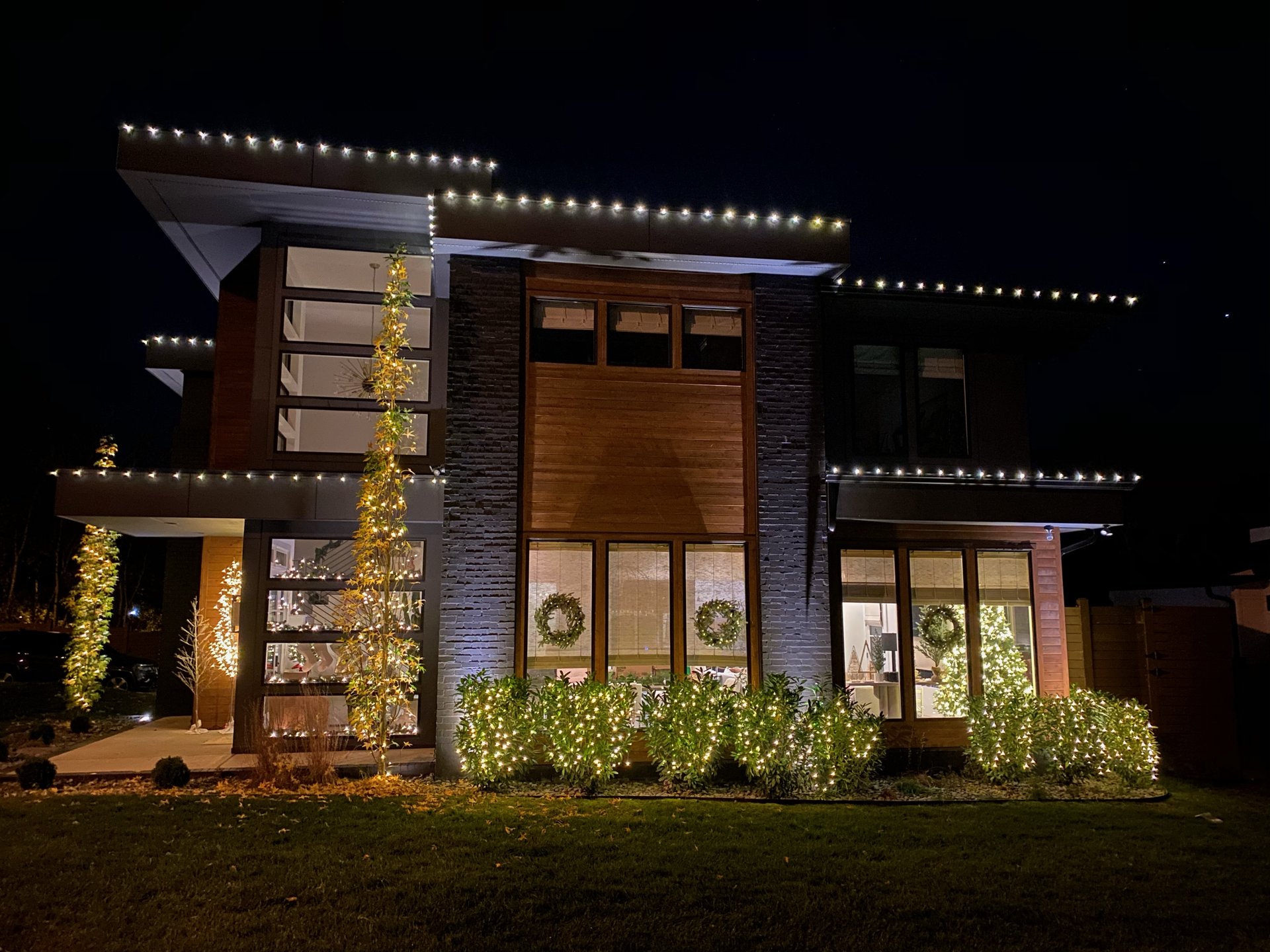 Modern home with wrapped trees, wreaths, and roofline lighting