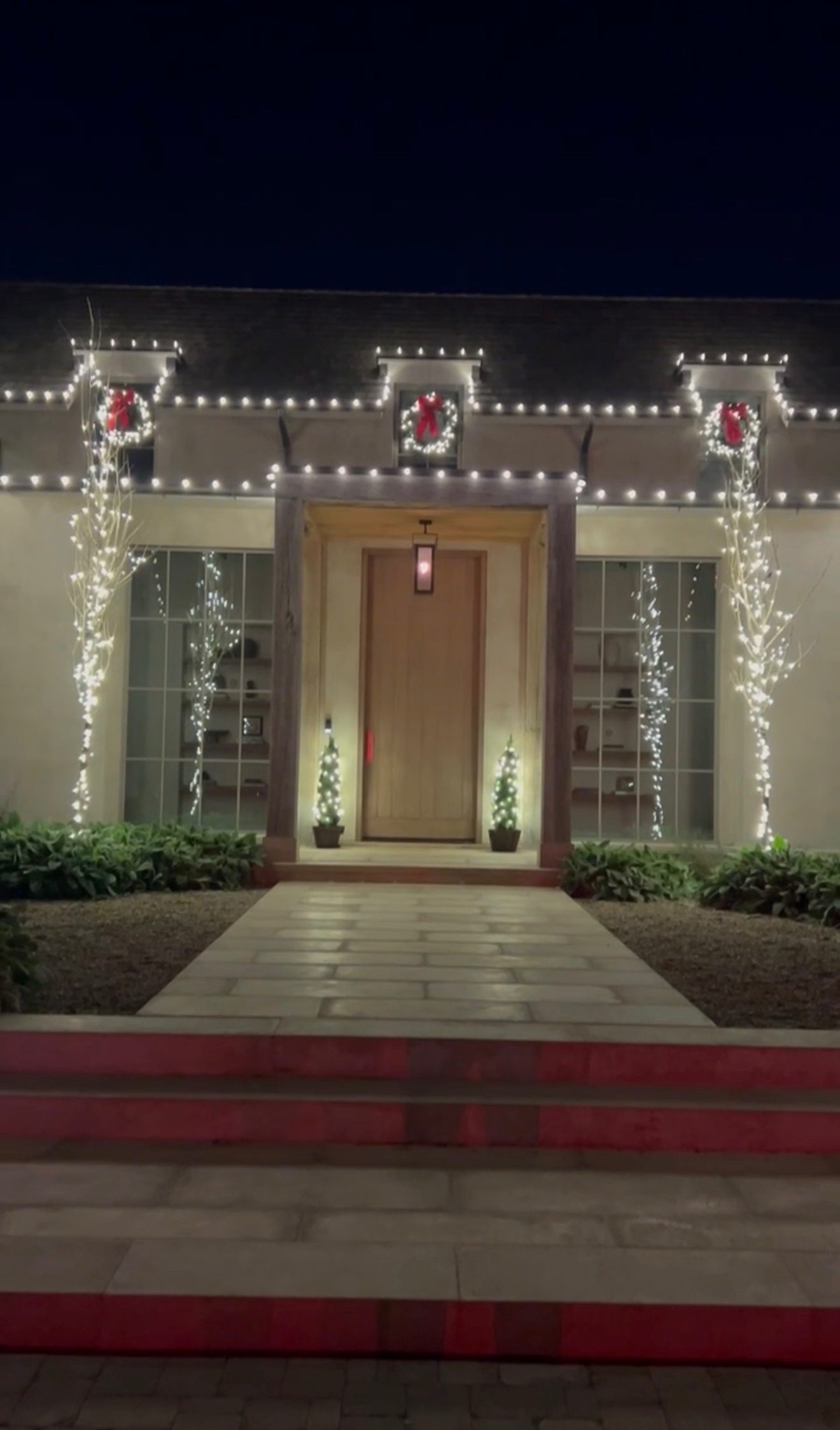 Three lit wreaths with red bows over a modern entryway